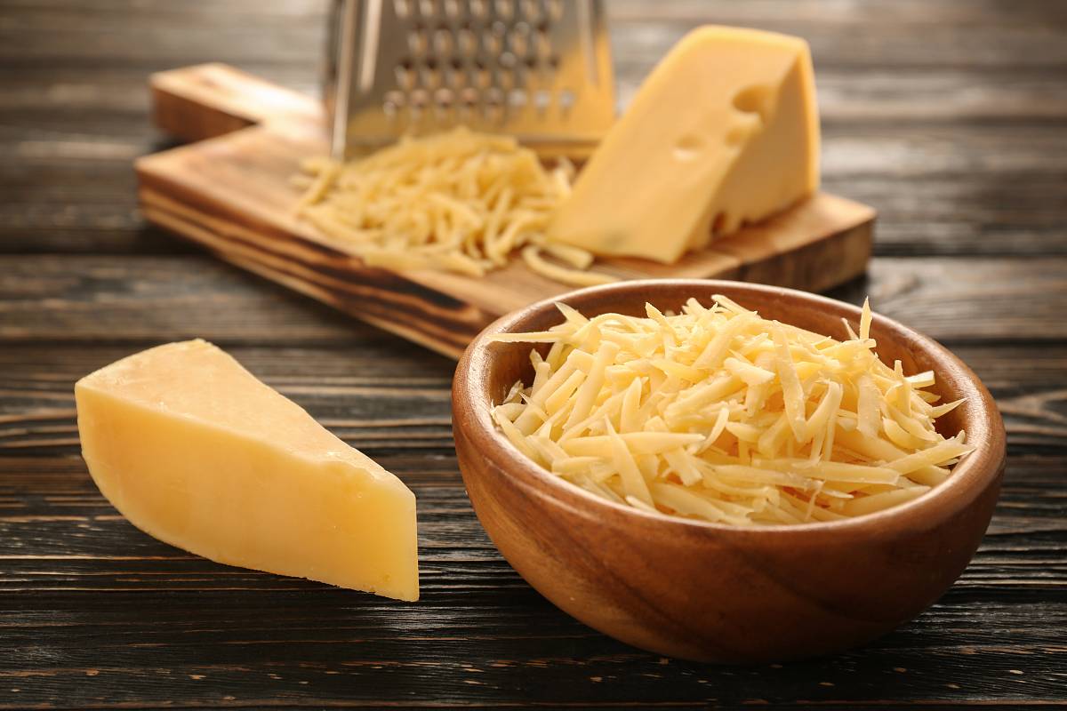 Reibkäse in einer Schüssel und auf einem Brett, daneben zwei Käsestücke und eine Reibe