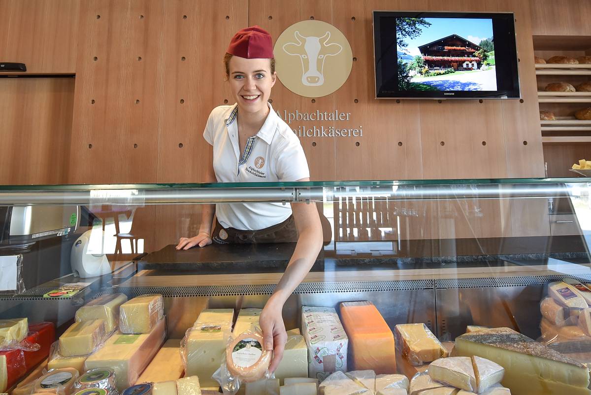 Eine Frau steht hinter der Ladentheke und hält Käse in der Hand.